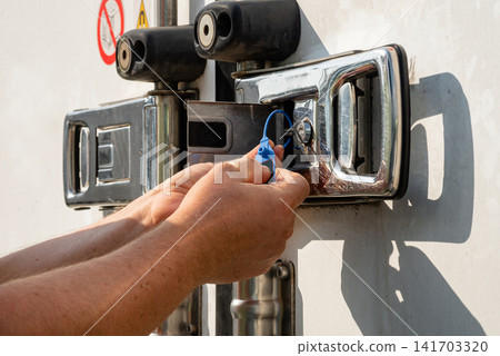 Hands of a worker installing a plastic security seal on a truck door Hands of a worker installing a plastic security seal on a truck door 141703320