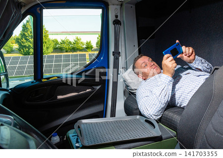 Exhausted commercial van driver lying down and looking at his smartphone Exhausted commercial van driver lying down and looking at his smartphone 141703355