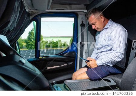 Professional courier looking at his phone inside a commercial delivery van Professional courier looking at his phone inside a commercial delivery van 141703356