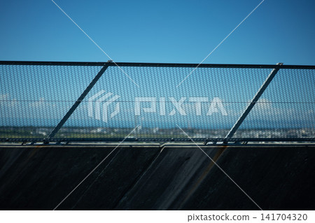 Wire mesh fence, blue sky, and a distant cityscape. Wire mesh fence, blue sky, and a distant cityscape. 141704320