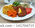 Traditional schnitzel served with french fries, grated carrots, spaetzle, and salad garnish 141704715