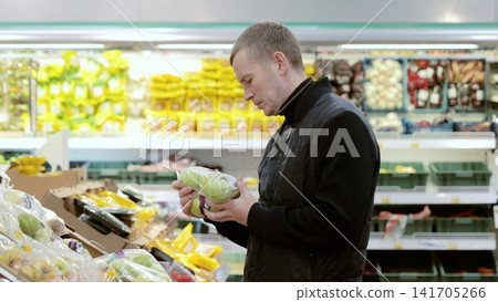 Man choosing apples at grocery store, reading labels for healthy options. Fresh produce display with vibrant colors. Everyday consumer experience in bustling supermarket aisle Man choosing apples at grocery store, reading labels for healthy options. Fresh produce display with vibrant colors. Everyday consumer experience in bustling supermarket aisle 141705266