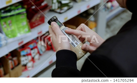 A customer in black studies the label on a bottle of sauce. Shopper compares the nutritional labels of various grocery store items while shopping A customer in black studies the label on a bottle of sauce. Shopper compares the nutritional labels of various grocery store items while shopping 141705294