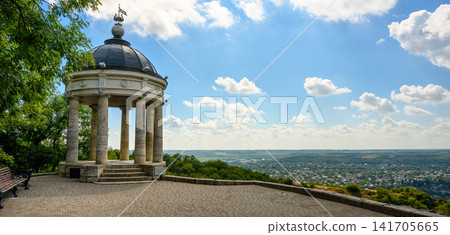 Classical stone rotunda on an elevated observation deck, Pyatigorsk, Russia. Panoramic viewpoint overlooking a town in a green valley. Summer landscape with blue sky and clouds in background Classical stone rotunda on an elevated observation deck, Pyatigorsk, Russia. Panoramic viewpoint overlooking a town in a green valley. Summer landscape with blue sky and clouds in background 141705665