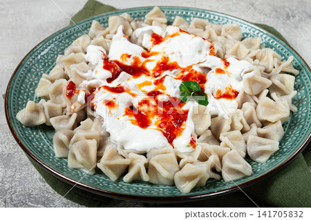 Traditional Turkish dumplings served with yogurt and spicy sauce on a green decorative plate Traditional Turkish dumplings served with yogurt and spicy sauce on a green decorative plate 141705832