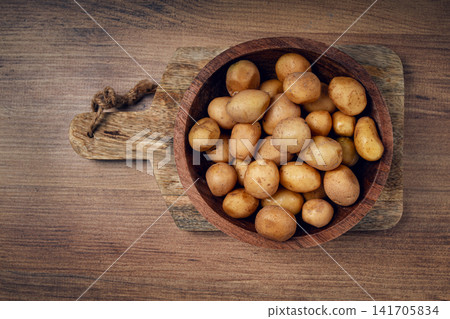 Freshly harvested small potatoes in a wooden bowl on a rustic cutting board Freshly harvested small potatoes in a wooden bowl on a rustic cutting board 141705834