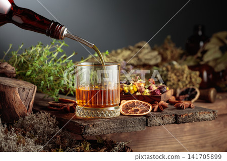Herbal bitter liqueur is poured from a vintage bottle into a glass. Herbal bitter liqueur is poured from a vintage bottle into a glass. 141705899