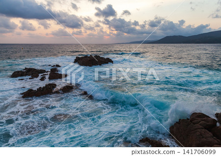 Black rocks are in shore waters at sunset. Coastal landscape of Propriano, Corsica Black rocks are in shore waters at sunset. Coastal landscape of Propriano, Corsica 141706099