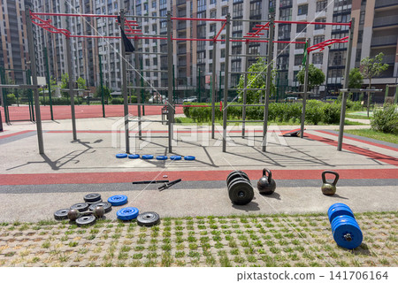 Modern outdoor fitness park with calisthenics bars, dumbbells, kettlebells and strength training equipment in a residential courtyard. Healthy lifestyle, functional training, sport and wellness. Modern outdoor fitness park with calisthenics bars, dumbbells, kettlebells and strength training equipment in a residential courtyard. Healthy lifestyle, functional training, sport and wellness. 141706164