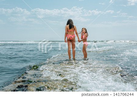 Two Sisters Holding Hands Walking towards the Sea, smaller sister looking at camera Two Sisters Holding Hands Walking towards the Sea, smaller sister looking at camera 141706244