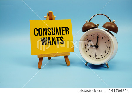 Consumer Wants text written on paper card and alarm clock on blue background Consumer Wants text written on paper card and alarm clock on blue background 141706254