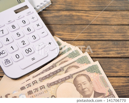 Copy space for a 10,000 yen bill and a calculator with a wood grain background. Copy space for a 10,000 yen bill and a calculator with a wood grain background. 141706770