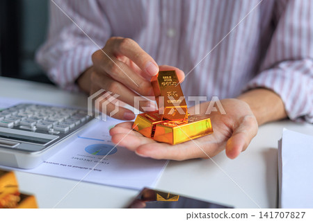 Physical gold bars on investor's hand at office desk. Concept for secure financial investment and wealth preservation. 141707827