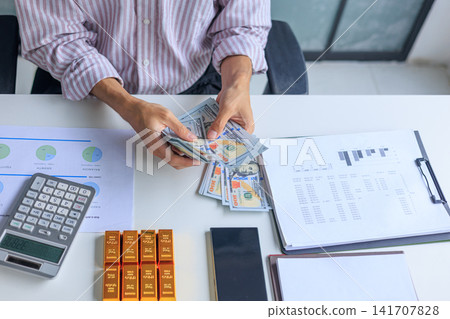 Banker, Accountant or Investor Counting Money with Gold Bars on the Table. Gold Commodity Trading and Market Analysis in Modern Office. 141707828