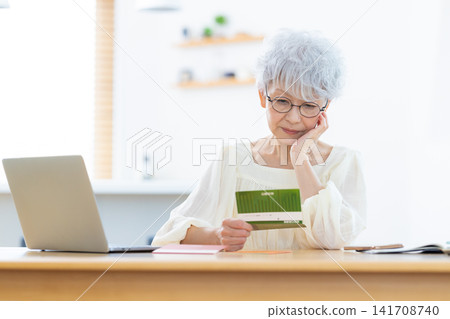 A senior woman looking at her bankbook in the living room A senior woman looking at her bankbook in the living room 141708740