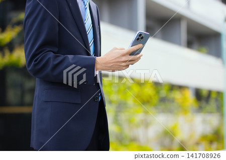 一位二十多歲的商人手持智慧型手機在戶外。 141708926