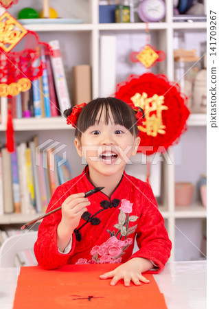 Little Asian Girl Writing Chinese Calligraphy Fai Chun for New Year Decoration,The text on the pendant hanging at the back reads: "Happy New Year." Little Asian Girl Writing Chinese Calligraphy Fai Chun for New Year Decoration,The text on the pendant hanging at the back reads: "Happy New Year." 141709267