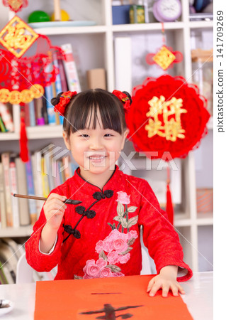 Little Asian Girl Writing Chinese Calligraphy Fai Chun for New Year Decoration,The text on the pendant hanging at the back reads: "Happy New Year." Little Asian Girl Writing Chinese Calligraphy Fai Chun for New Year Decoration,The text on the pendant hanging at the back reads: "Happy New Year." 141709269