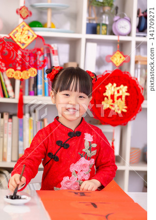 Little Asian Girl Writing Chinese Calligraphy Fai Chun for New Year Decoration,The text on the pendant hanging at the back reads: "Happy New Year." Little Asian Girl Writing Chinese Calligraphy Fai Chun for New Year Decoration,The text on the pendant hanging at the back reads: "Happy New Year." 141709271