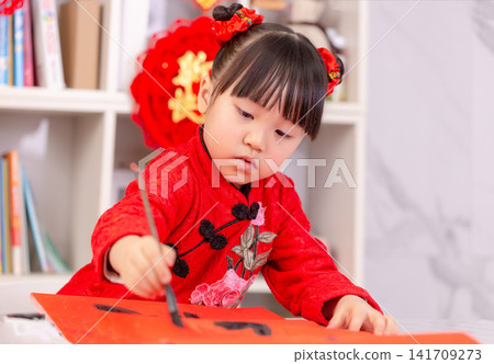 Little Asian Girl Writing Chinese Calligraphy Fai Chun for New Year Decoration,The text on the pendant hanging at the back reads: "Happy New Year." Little Asian Girl Writing Chinese Calligraphy Fai Chun for New Year Decoration,The text on the pendant hanging at the back reads: "Happy New Year." 141709273