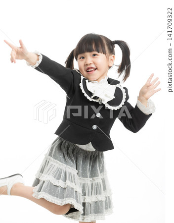 Energetic little girl in school uniform jumping with joy and gesturing success, white background. 141709322