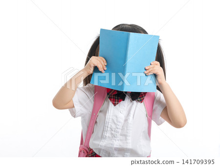 Shy Asian schoolgirl hiding her face behind a blue book, curiosity and reading concept. Shy Asian schoolgirl hiding her face behind a blue book, curiosity and reading concept. 141709395