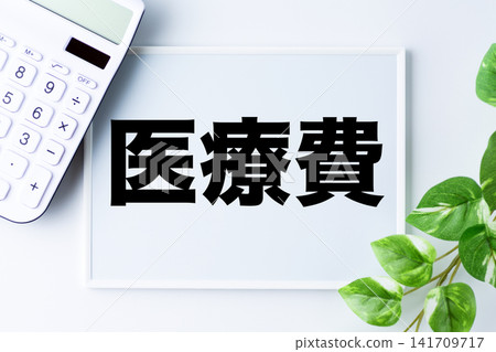一塊寫著「醫療費用」字樣的白板和一個白色計算器。 一塊寫著「醫療費用」字樣的白板和一個白色計算器。 141709717