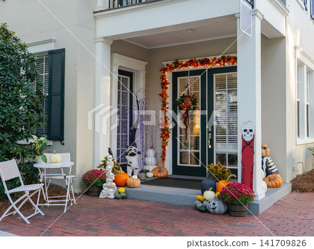 A residential front entrance is decorated with pumpkins, flowers, skeletons, lights, and seasonal Halloween ornaments. The festive autumn display creates a welcoming holiday atmosphere outside the 141709826