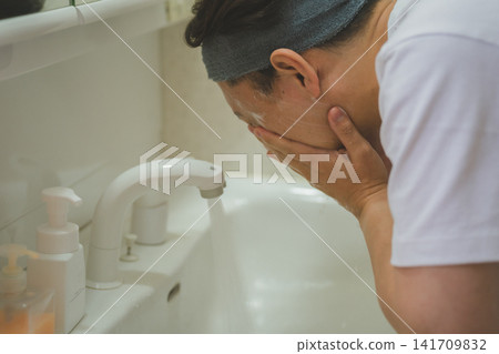 A 40-year-old man's skincare routine: carefully rinsing his face in both hands at the sink. A 40-year-old man's skincare routine: carefully rinsing his face in both hands at the sink. 141709832