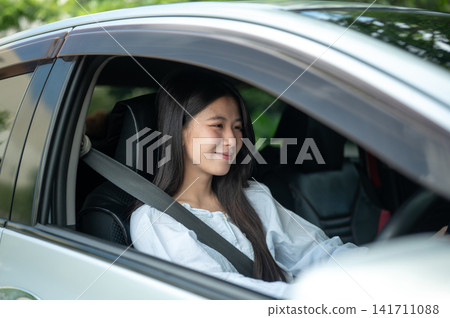 Young Asian woman seated comfortably while driving a car wearing seatbelt behind the steering wheel. Young Asian woman seated comfortably while driving a car wearing seatbelt behind the steering wheel. 141711088