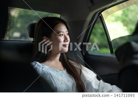 Young Asian woman enjoying a ride while looking out of car window in the back seat of a taxi cab car 141711093