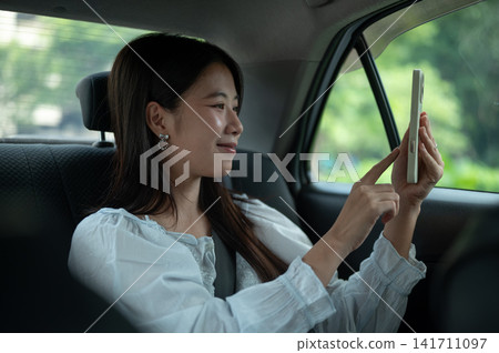 Young Asian woman taking a selfie photo with smartphone while sitting in back seat of a taxi cab car Young Asian woman taking a selfie photo with smartphone while sitting in back seat of a taxi cab car 141711097
