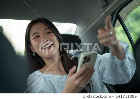 Young Asian woman giving a direction to driver while traveling in the back seat of a taxi cab car. 141711099