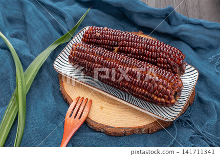 boiled black sticky corn on cobs served on a plate isolated on white background boiled black sticky corn on cobs served on a plate isolated on white background 141711341
