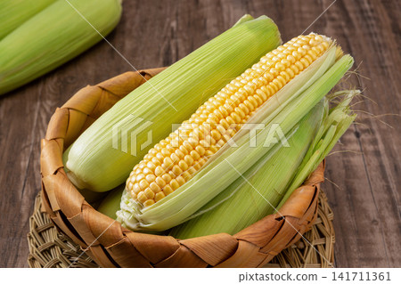 fresh green sweet corn with husks and cooked corn segments on plate fresh green sweet corn with husks and cooked corn segments on plate 141711361