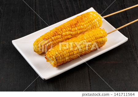 grilled sweet corn on wooden skewers served on a white plate grilled sweet corn on wooden skewers served on a white plate 141711564