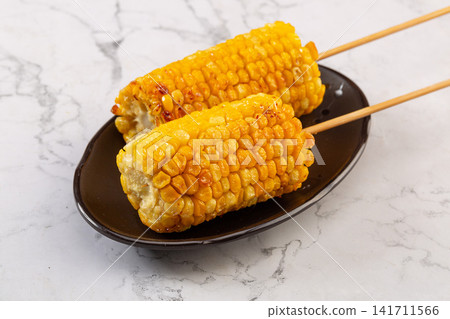 grilled sweet corn on wooden skewers served on a white plate 141711566