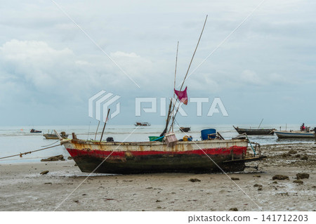 Small traditional wooden fishing boat resting on sandy beach at low tide with sea background Small traditional wooden fishing boat resting on sandy beach at low tide with sea background 141712203