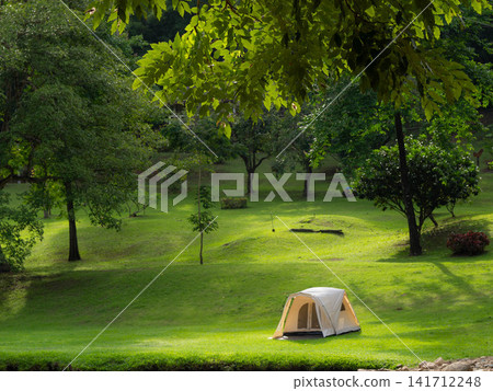 White camping tent set up on a lush green lawn surrounded by big trees in a quiet park White camping tent set up on a lush green lawn surrounded by big trees in a quiet park 141712248
