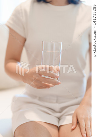 Healthy woman hold glass of clean mineral water glass on sofa at home, female drink pure water for hydration and wellness, fresh skin care, daily routine water intake, Refreshment and lifestyle Healthy woman hold glass of clean mineral water glass on sofa at home, female drink pure water for hydration and wellness, fresh skin care, daily routine water intake, Refreshment and lifestyle 141713289