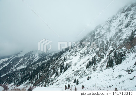 Snow blankets mountainous terrain under misty clouds Snow blankets mountainous terrain under misty clouds 141713315