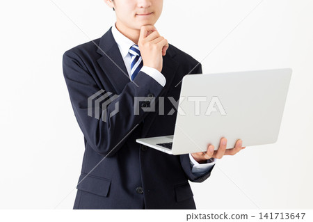 A young businessman in a suit is seen looking at his laptop and pondering. A young businessman in a suit is seen looking at his laptop and pondering. 141713647