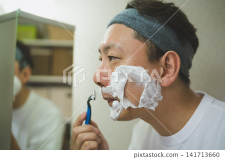 A 40-year-old man's morning shave: applying shaving foam to the area under his nose and using a T-shaped razor. A 40-year-old man's morning shave: applying shaving foam to the area under his nose and using a T-shaped razor. 141713660