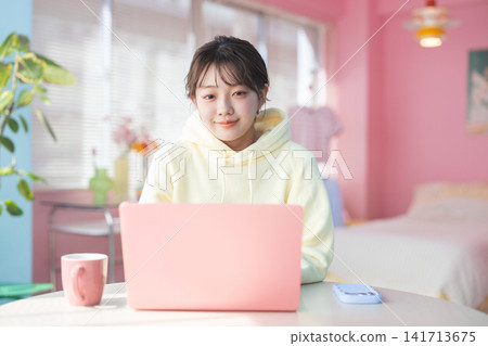 一位年輕女子微笑地打開她在家裡的筆記型電腦——她正在家工作。 一位年輕女子微笑地打開她在家裡的筆記型電腦——她正在家工作。 141713675