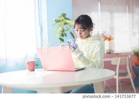 A young woman opens her laptop and operates her smartphone. A young woman opens her laptop and operates her smartphone. 141713677