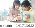 A young woman talking to a friend while looking at her smartphone. 141713682