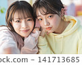Two young women lean in close, smiling and looking at the camera. 141713685