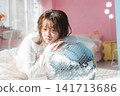 A young woman leans against a disco ball, gazing with an ennui expression. 141713686