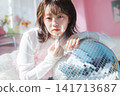 A young woman leans against a disco ball, applying lipstick with an ennui expression. 141713687