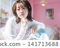 A young woman applies lipstick with an ennui expression. 141713688